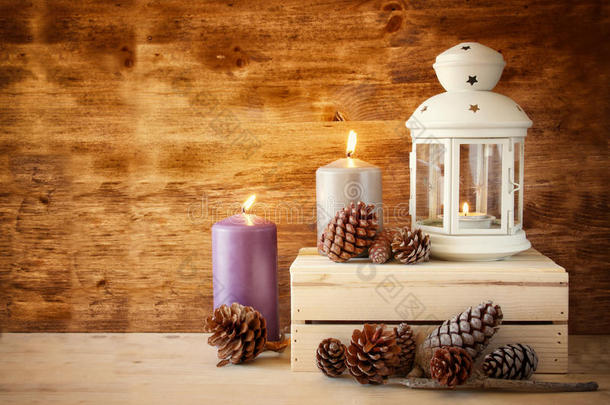 木制桌子上有燃烧的蜡烛和松果的老式灯笼。过滤后的图像