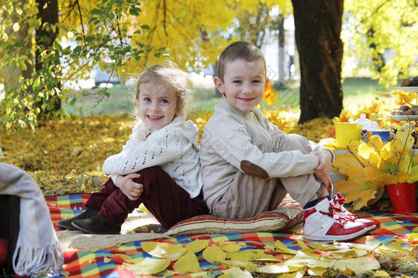 妹妹和弟弟背靠背坐在秋树下