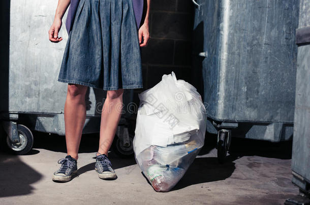 站在垃圾桶旁边的女人拿着一袋垃圾