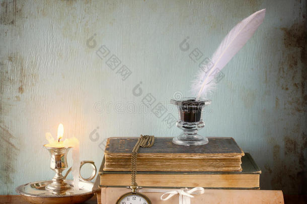 在旧木桌上低调地画着白羽毛、墨水池和蜡烛。图像纹理。