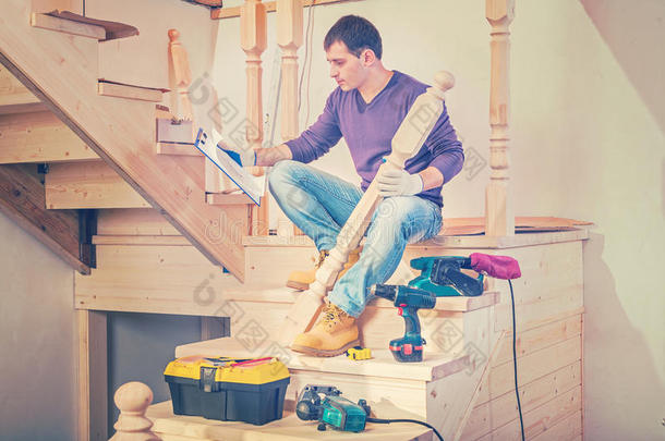 一个年轻的建筑承包商坐在木梯的台阶上，在剪贴板InstagramStile中寻找蓝图