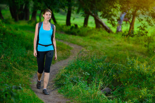 年轻美丽的女人在绿色的夏日森林里徒步旅行