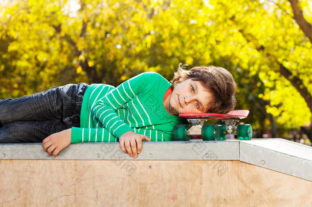 穿着绿色毛衣的小男孩躺在滑板上
