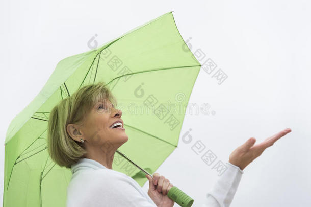 在晴朗的天空下，带着绿色雨伞的女人在享受雨天