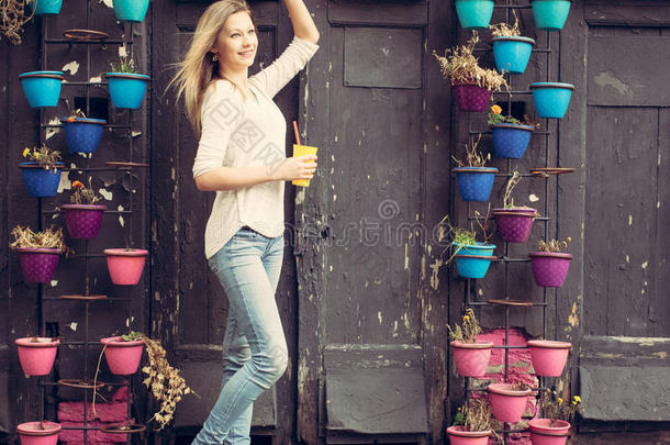 穿着牛仔裤和<strong>运动鞋</strong>的女孩拿着一个黄色的杯子在墙上挥舞着鲜花。<strong>户外</strong>的