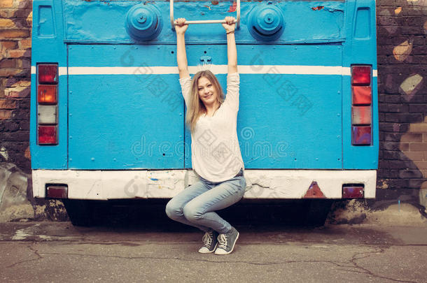 穿着牛仔裤和<strong>运动鞋</strong>的女孩在旧公共汽车附近摆姿势。<strong>户外</strong>的