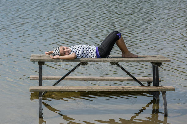 快乐快乐的小女孩躺在湖边野餐桌上放松