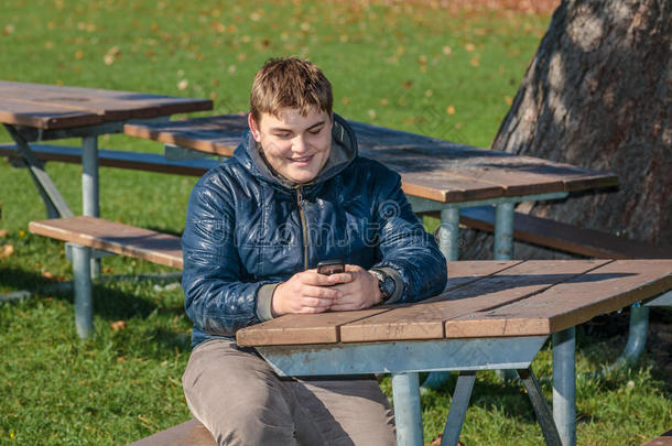 快乐的小男孩坐在秋天的公园里放松，用手机发短信