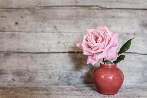 红色花瓶里的粉红色玫瑰，背景是旧木头