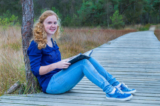 在森林里的木小路上看书的女孩