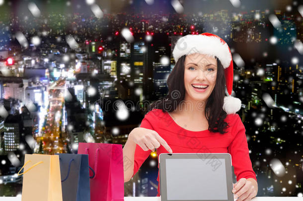 带着圣诞帽的微笑的女人带着<strong>袋子</strong>和平板电脑