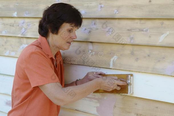 一<strong>位</strong>中年妇女在用砂纸打磨<strong>挡</strong>雨板上的油漆。