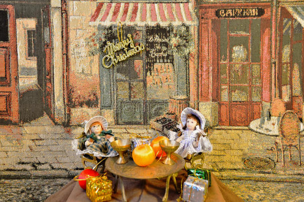 装饰：两个漂亮的洋娃娃坐在餐厅附近的桌子上，在艺术挂毯的衬托下摆放着圣诞礼物
