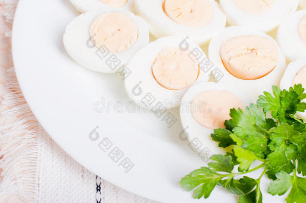 煮鸡蛋切成两半，放在一个白色盘子里，餐巾上放着欧芹，放在一张浅木的桌面上