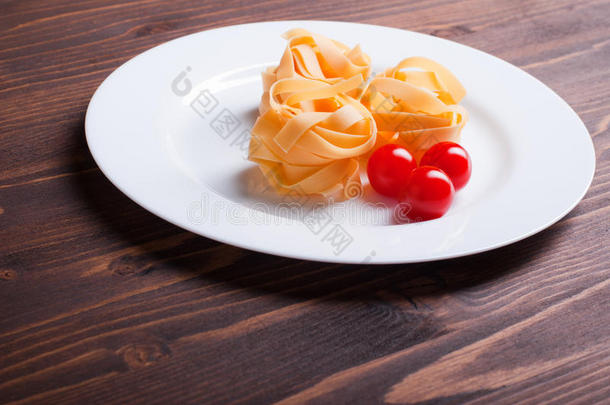 生面食<strong>三个</strong>圆和<strong>三个</strong>樱桃西红柿放在一<strong>个</strong>白色盘子上，棕色木制桌面俯视图