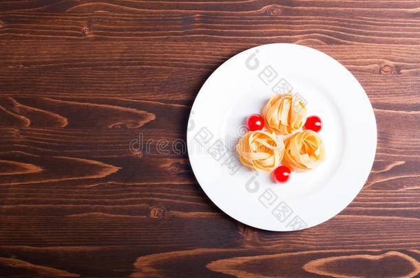 生面食三个圆和三个樱桃西红柿放在一个白色盘子上，棕色木制桌面俯视图