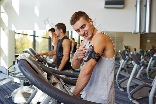 带着智能手机的男人在健身房的跑步机上锻炼