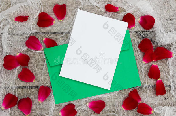 节日贺卡信封和带有玫瑰花瓣的信，背景为古董网和木质背景