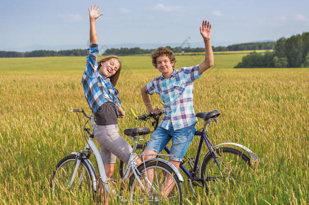一对十几岁的女孩和男孩骑着自行车在夏天的麦田里