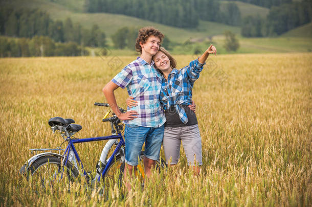 一对十几岁的女孩和男孩骑着自行车在夏天的麦田里
