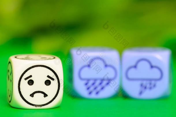 悲伤风暴天气的概念-绿色背景上的表情符号和天气骰子