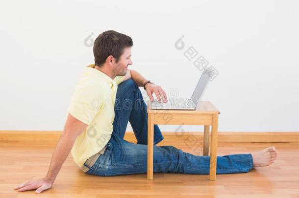 在家里咖啡桌上用笔记本电脑坐在地板上的休闲男人