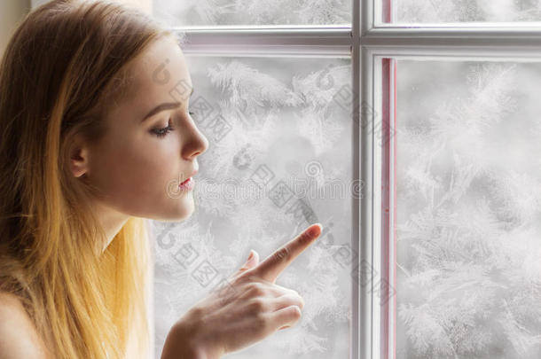 美丽的年轻女孩坐在<strong>窗边</strong>的冬日，在冰冻的<strong>窗</strong>户上画着太阳
