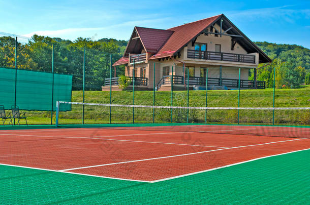 网球场，后面是一个美丽的小屋，四周是树木和山丘