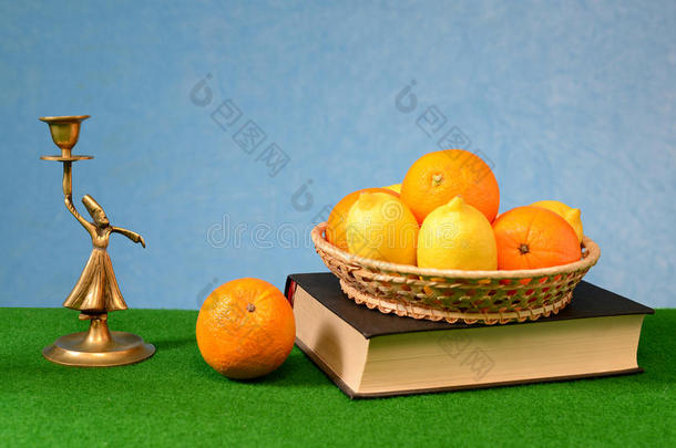 柳条篮子里的柑橘类水果，放在一个<strong>古铜</strong>雕像旁边的书上