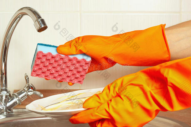 手戴手套拿着脏盘子放在厨房的水槽上