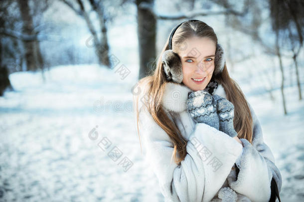 穿着耳罩、针织手套和毛皮<strong>大衣</strong>的漂亮女人在<strong>冬天</strong>的森林里玩得很开心