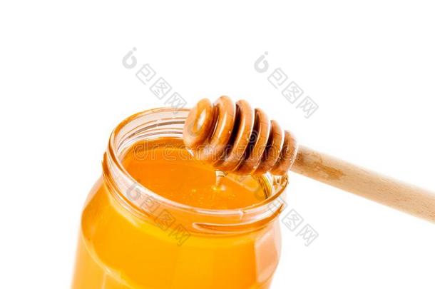 打开的<strong>蜂蜜</strong>罐在白色的背景上，上面有木制的<strong>蜂蜜</strong>勺，上面倒着<strong>蜂蜜</strong>