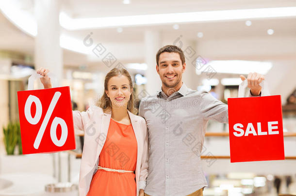 一对快乐的年轻夫妇拿着红色的购物袋在购物中心