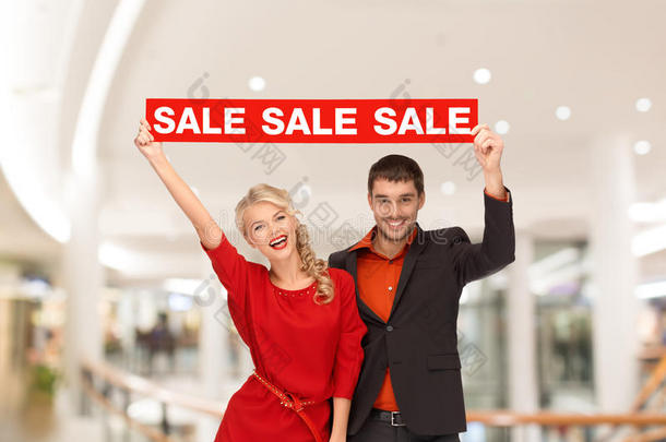 一对快乐的年轻夫妇拿着红色的购物袋在购物中心