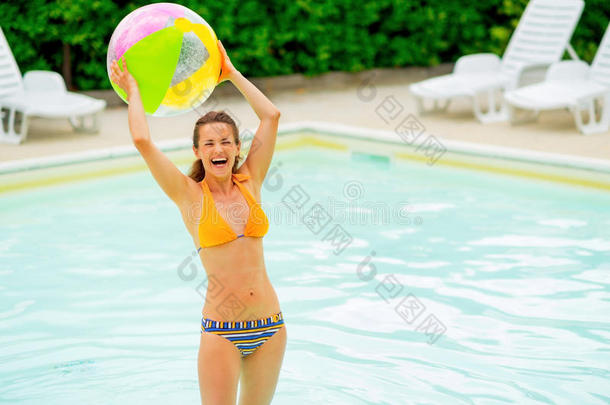 游<strong>泳池</strong>里带着<strong>沙滩</strong>球微笑的年轻女子