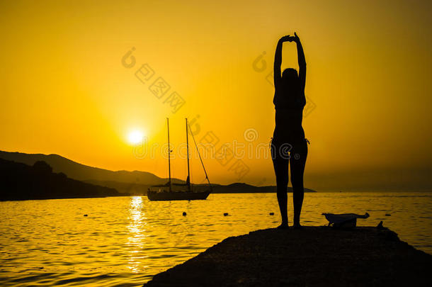 日落时在海滩上练瑜伽的女孩