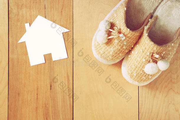顶视图温暖的妇女拖鞋超过木地板和纸房子形状作为欢迎回家的概念