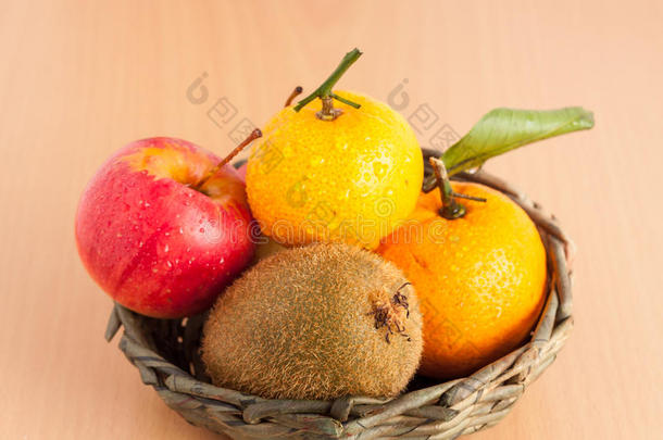 成熟的红苹果，猕猴桃和橘子放在夹板背景的篮子里