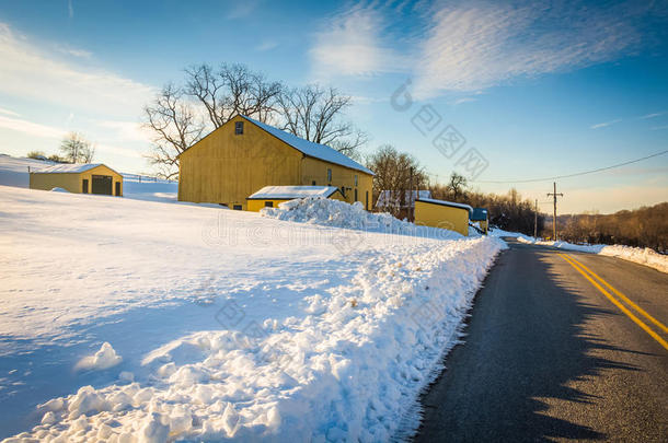 宾夕法尼亚州约克县一条乡间小路旁的黄色谷仓和一片白雪覆盖的田野。