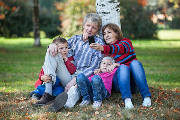 爷爷奶奶和孙子孙女坐在一起，在公园里用手机自拍