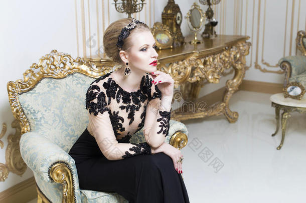 美丽的金发皇家女子躺在复古沙发上华丽的豪华礼服