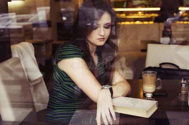 黑发女人坐在咖啡馆看书学习喝咖啡等待迟到