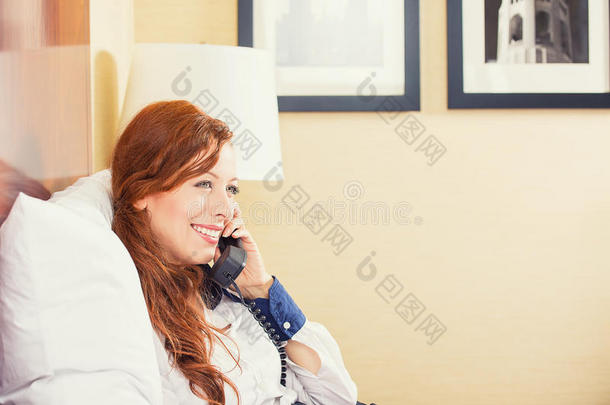 坐在酒店房间的床上，面带微笑的女商人在打电话。
