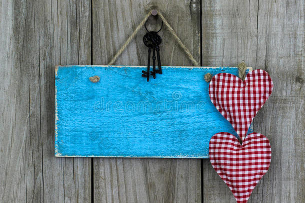空白的蓝色标牌，红色织物心形，铁钥匙挂在破旧的木质背景上
