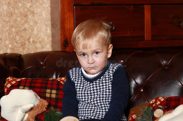一个穿着毛衣的小男孩坐在棕色沙发上