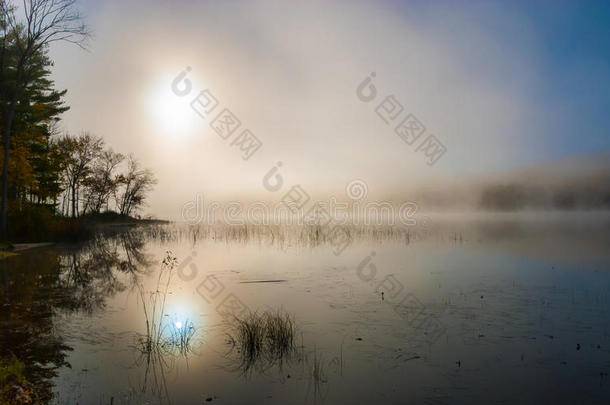 日出穿过湖面的晨雾。