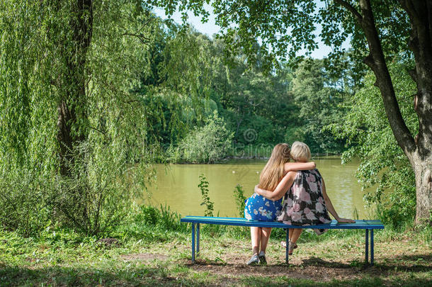 夏天，两个不同年代的女人坐在池塘边的长凳上。母女拥抱。奶奶和奶奶