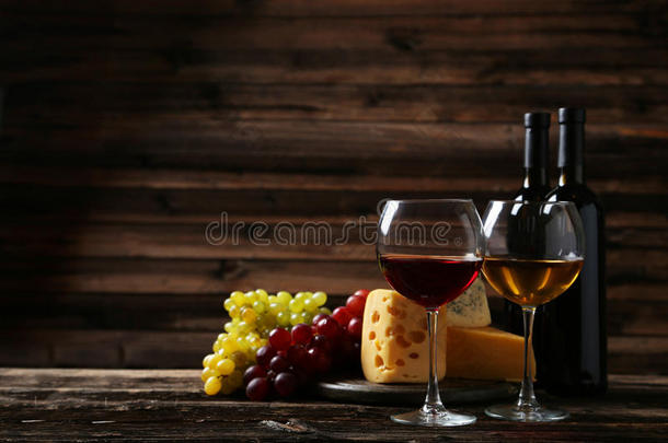 棕色木制背景上的一杯红白酒、奶酪和葡萄