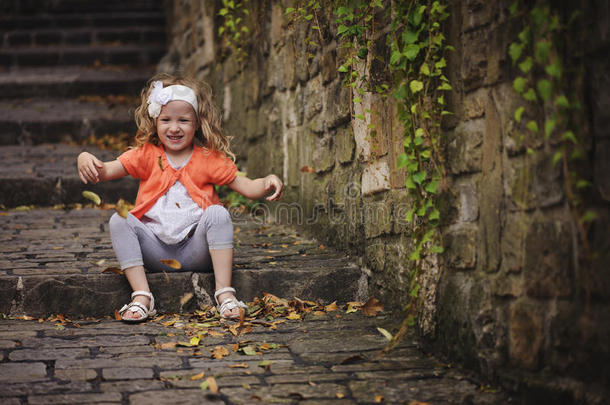 小女孩一边坐在旧石头楼梯上一边玩，一边扔树叶
