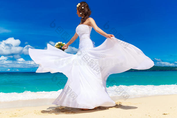 美丽的黑发新娘穿着白色婚纱，白色的大火车和婚礼花束站在海边。 热带地区